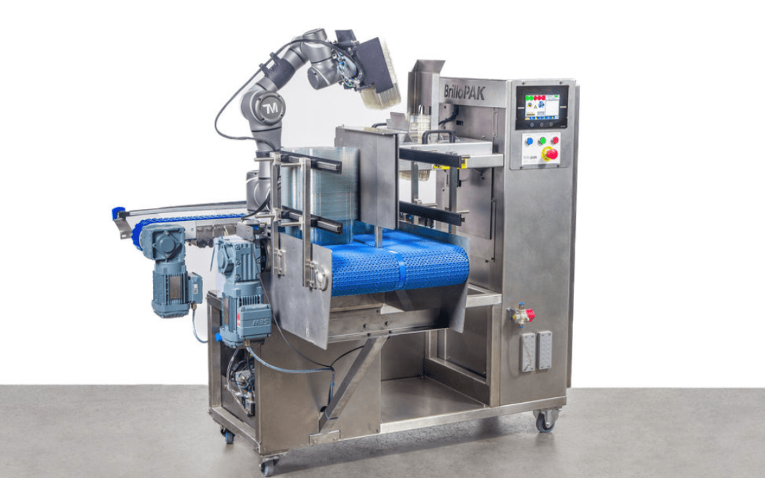 A close-up of a Brillopak automated denesting machine, showing a robotic arm with an end effector that precisely picks and places nested trays from a stack onto a blue conveyor belt.