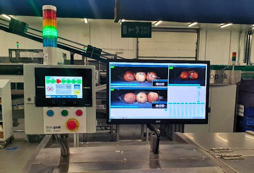 A close-up view of a Brillopak vision system console shows a computer monitor displaying three images of apples on a conveyor belt, as it checks product quality.