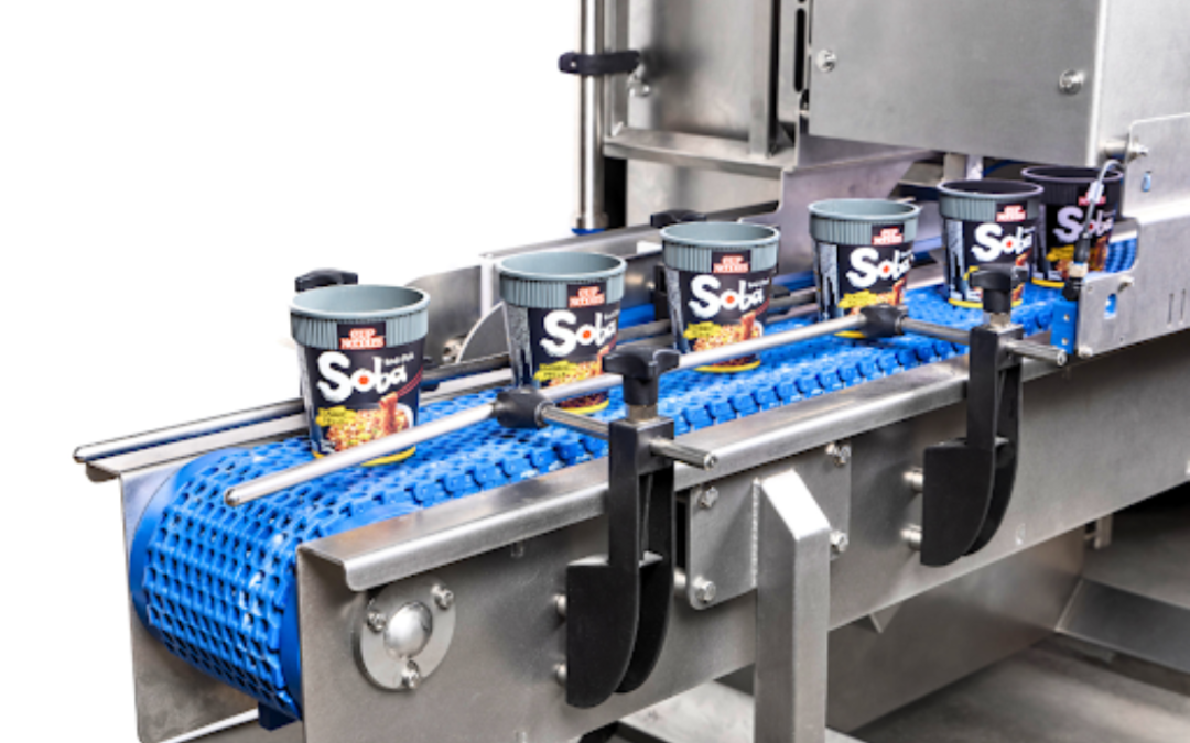 A line of ready-to-eat noodle cups moves along a blue conveyor belt, guided by automated machinery.